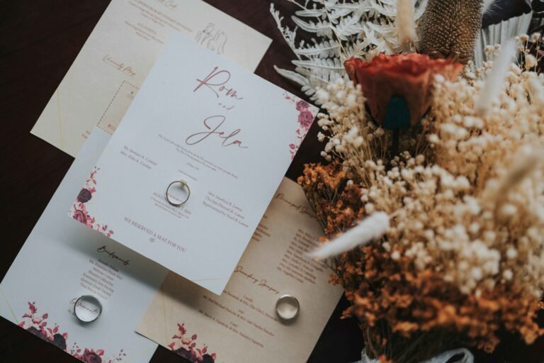 White and beige minimal wedding invitations with a ring placed on top of it. On the side there is a bouquet of white and burnt orange flowers.